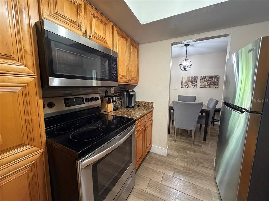 A kitchen with wood cabinets, stainless steel appliances, and tile flooring leads to a dining area — 4807 S TEXAS AVENUE UNIT 4807C, ORLANDO, FL