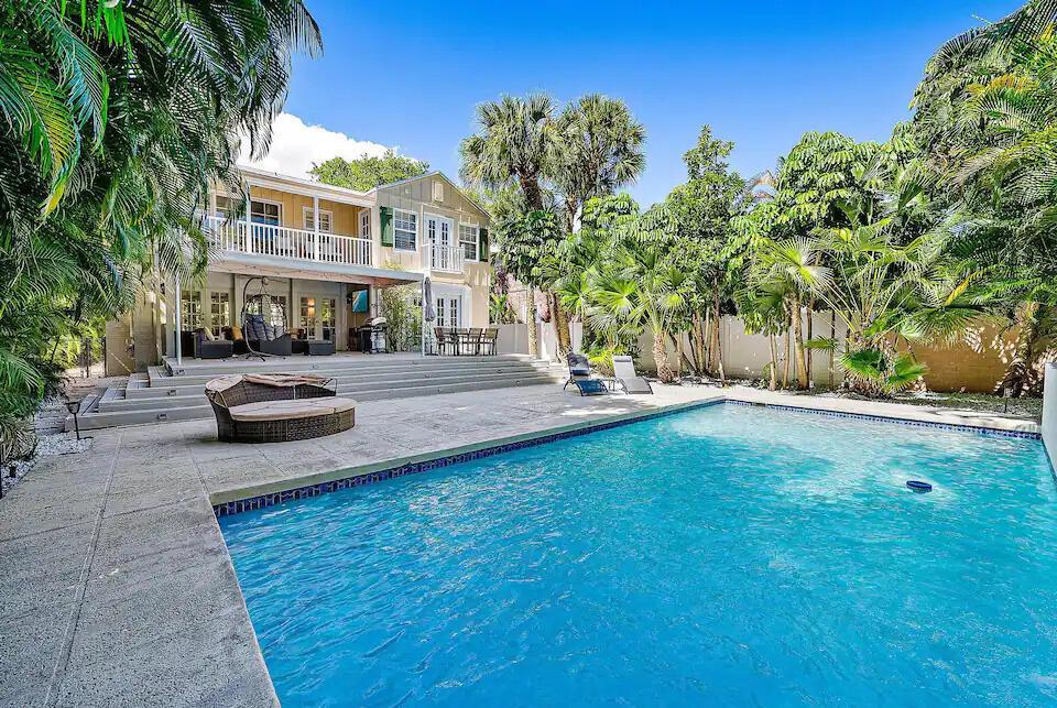 A two-story yellow house features a backyard swimming pool, stone patio, and lush palm trees — 4110 Washington Road, West Palm Beach FL 33405, WEST PALM BEACH, FL