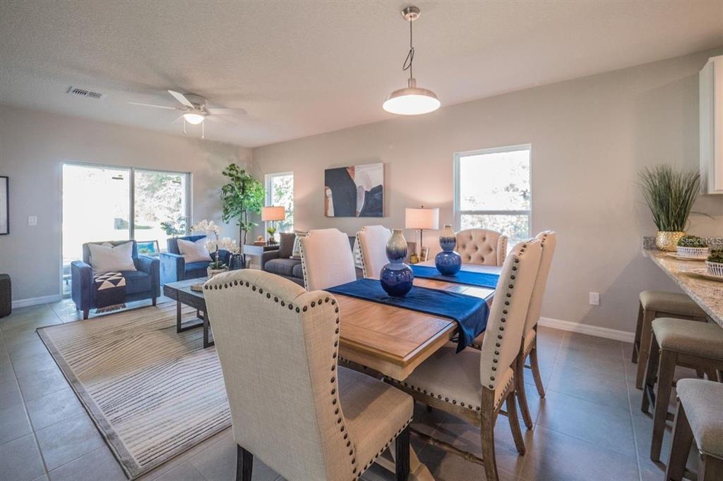 An open-concept dining and living area features a wooden table, upholstered chairs, and tile flooring — 1701 PILCHARD DRIVE, POINCIANA, FL