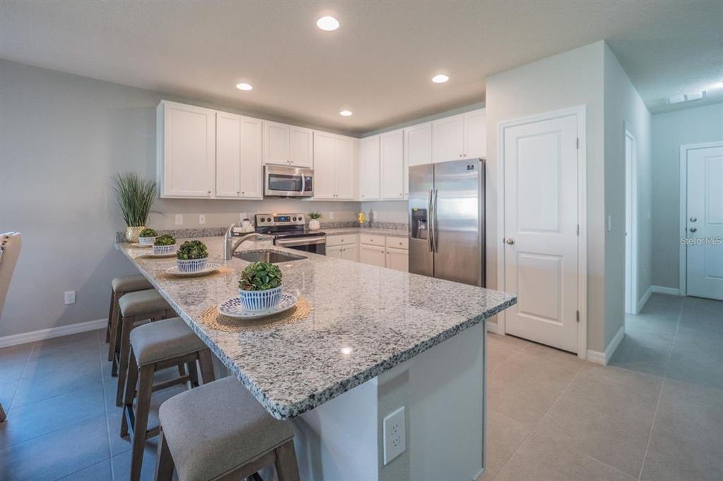 A kitchen features white cabinets, granite countertops, a large island, and stainless steel appliances — 1701 PILCHARD DRIVE, POINCIANA, FL