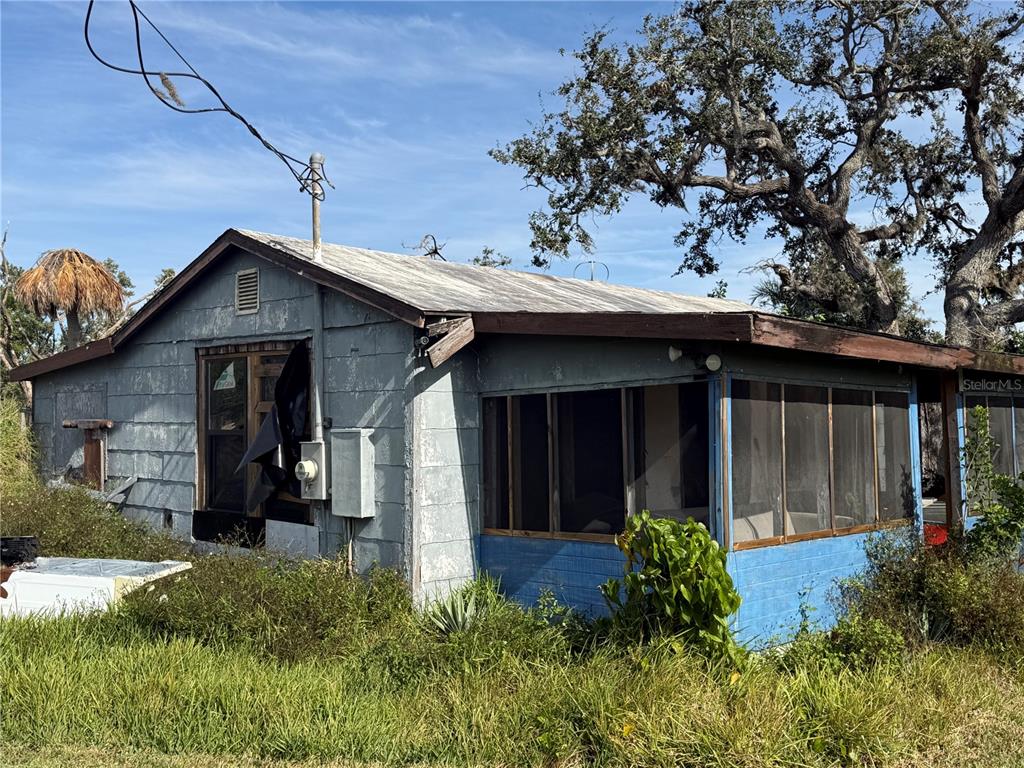 A weathered, single-story house with a screened-in porch and overgrown yard under a blue sky — 916 PINEY POINT ROAD, PALMETTO, FL