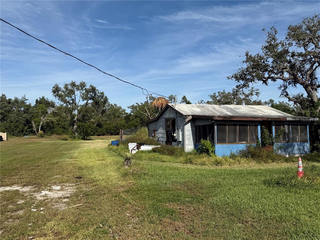 A weathered, single-story house with a screened porch sits on a large, grassy lot — 916 PINEY POINT ROAD, PALMETTO, FL