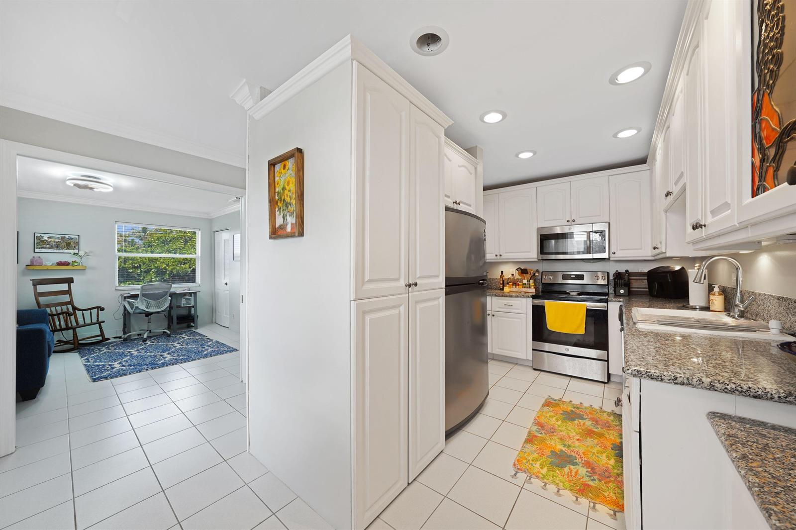 A white kitchen with stainless steel appliances and granite countertops opens into a home office — 2835 SW 13th Street # 201, Delray Beach FL 33445, DELRAY BEACH, FL