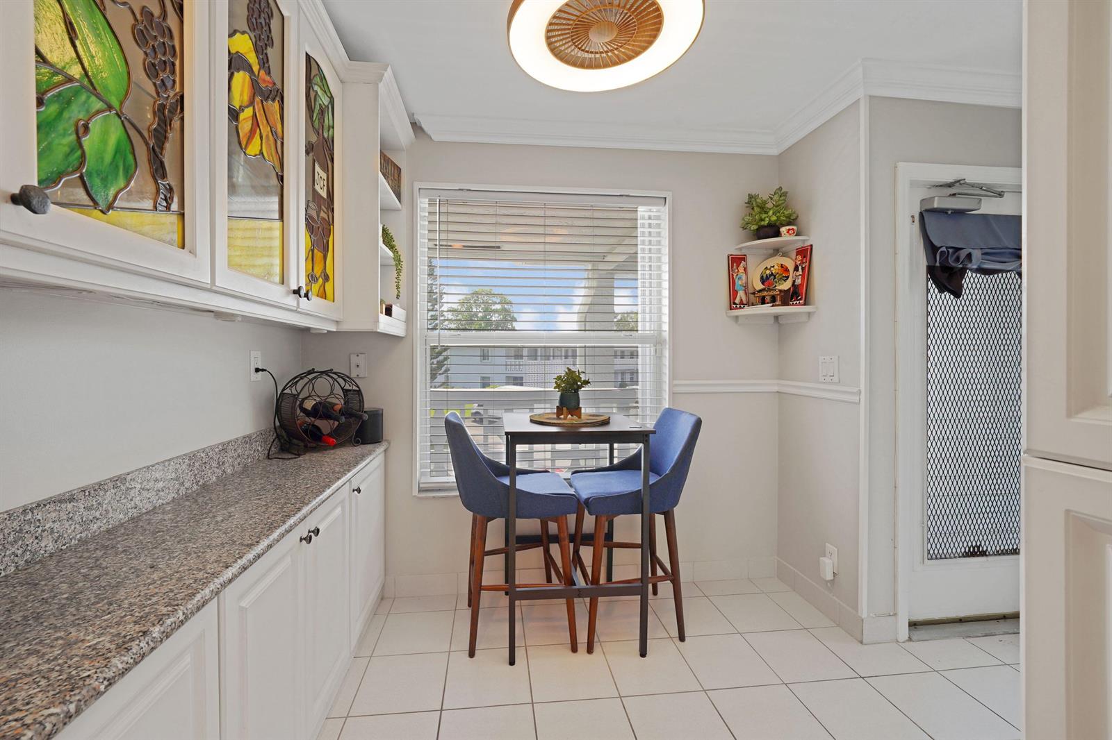 A kitchen dining area features white cabinets, stained glass accents, a small table, and two chairs — 2835 SW 13th Street # 201, Delray Beach FL 33445, DELRAY BEACH, FL