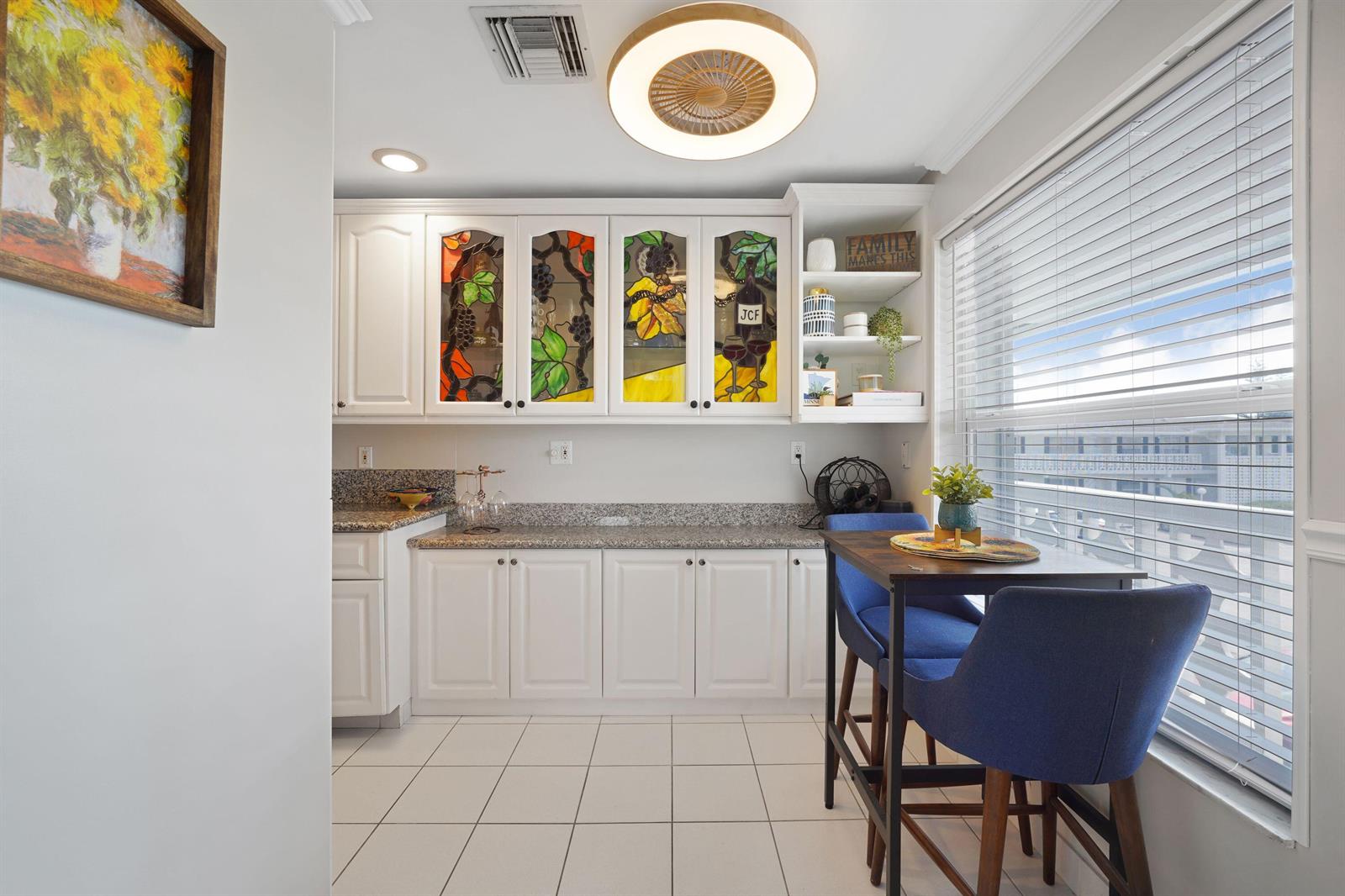 A kitchen area features white cabinets with stained glass inserts, granite countertops, and blue chairs — 2835 SW 13th Street # 201, Delray Beach FL 33445, DELRAY BEACH, FL