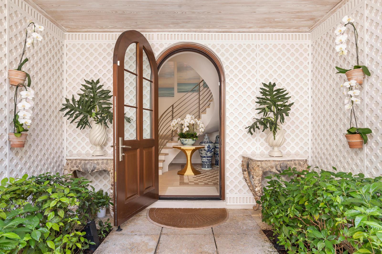 An arched wooden door opens to a foyer with a staircase and lattice-patterned walls — 5 Via Flagler, Palm Beach FL 33480, PALM BEACH, FL