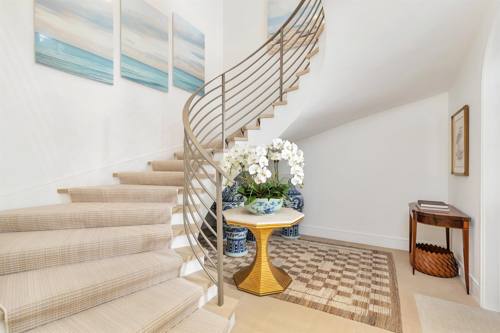 A curved staircase with a metal railing sits beside a foyer featuring a pedestal table — 5 Via Flagler, Palm Beach FL 33480, PALM BEACH, FL