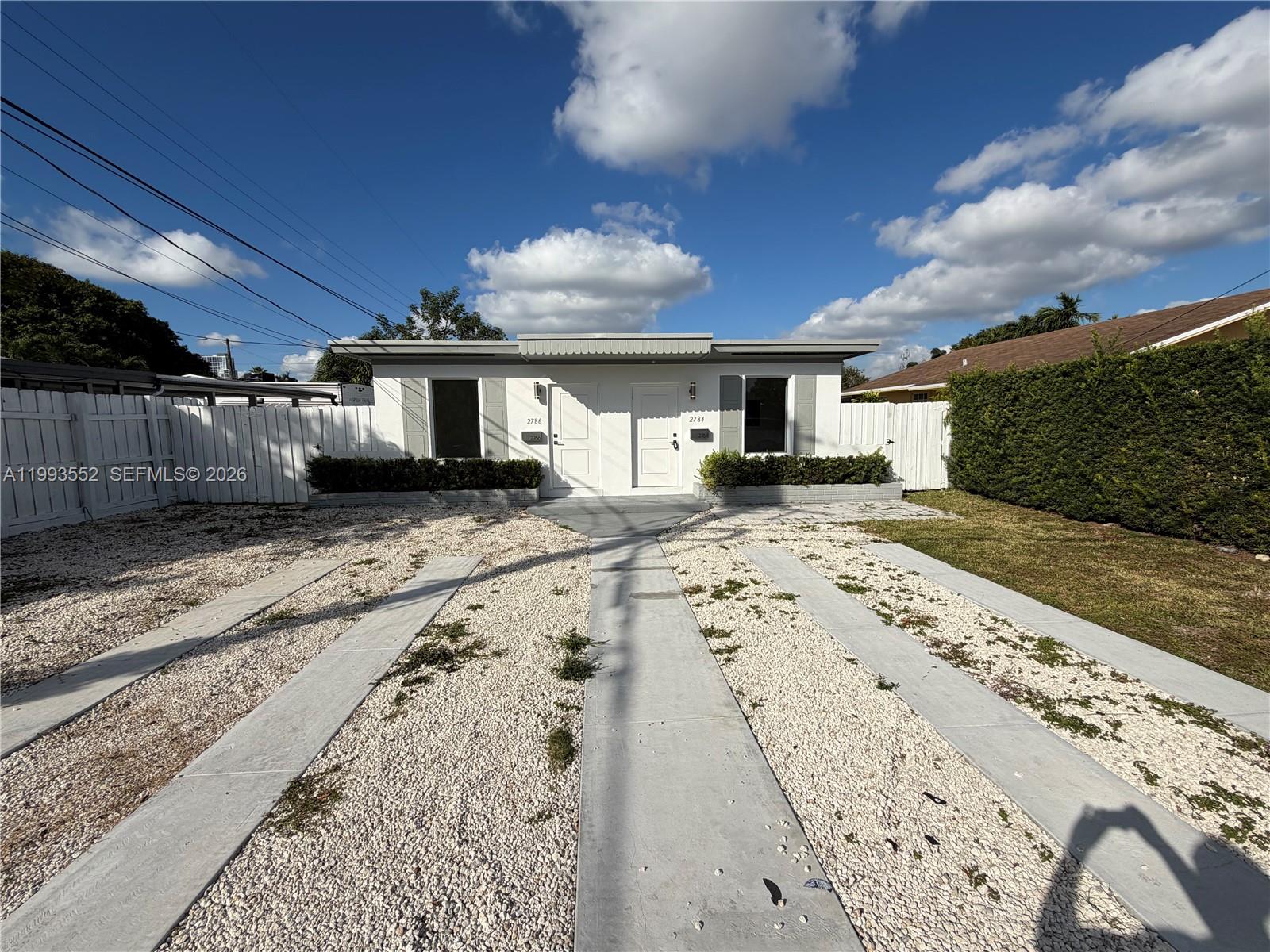 A single-story duplex with a gravel driveway and white fence under a blue sky — 2784 SW 31st Pl, Miami FL 33133, MIAMI, FL