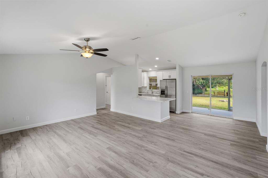 An open-concept living room with light wood-look flooring, a ceiling fan, and a kitchen area — 5108 WEATHERTON STREET, NORTH PORT, FL