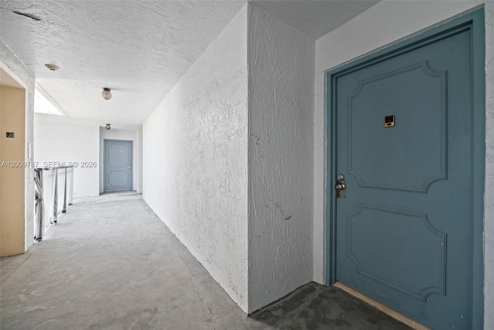 A concrete outdoor hallway features white textured walls and two blue paneled entry doors — 7751 NE Bayshore Ct # 7B, Miami FL 33138, MIAMI, FL