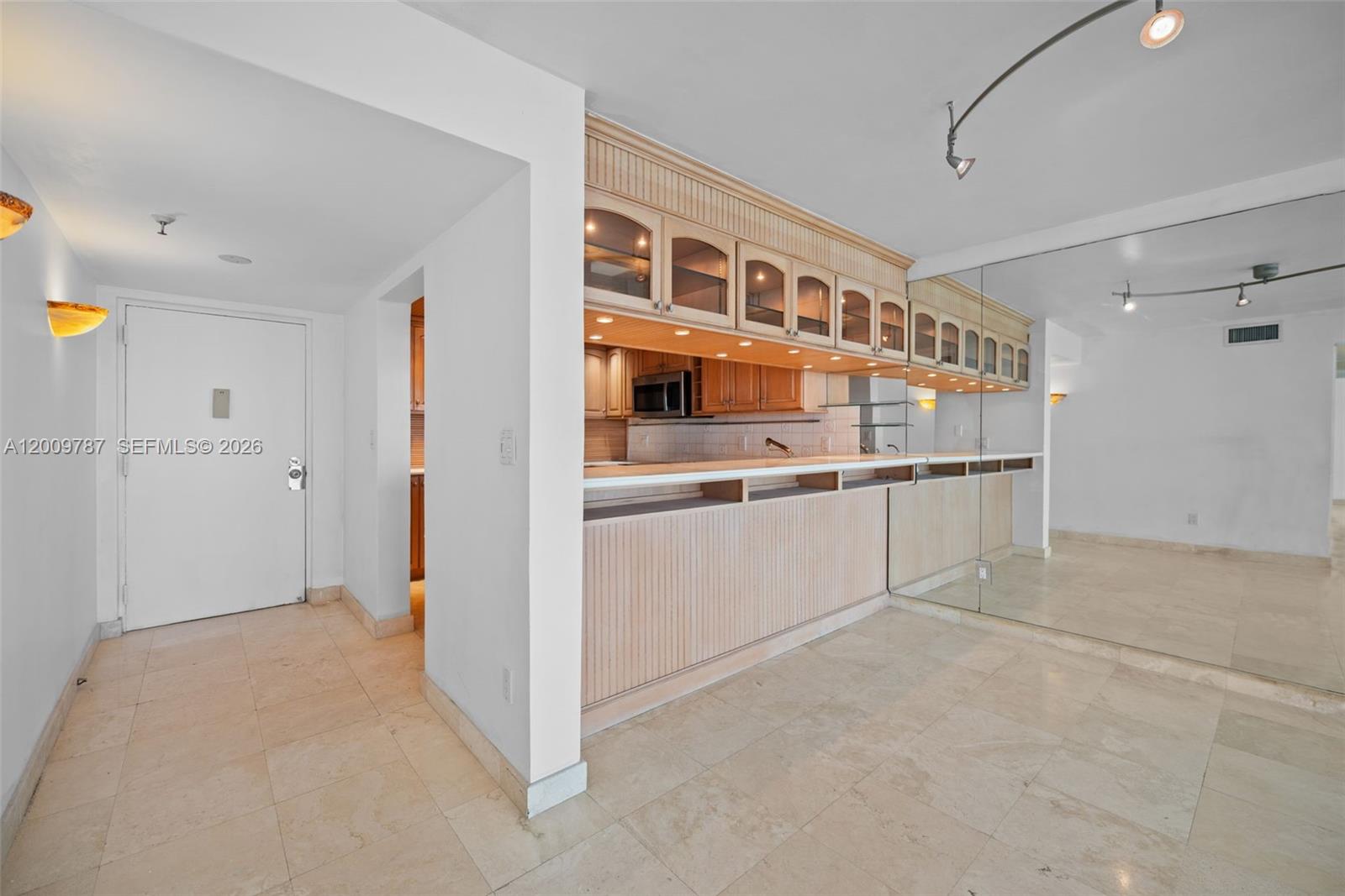 A kitchen features light wood cabinetry, a breakfast bar, and a mirrored wall — 7751 NE Bayshore Ct # 7B, Miami FL 33138, MIAMI, FL