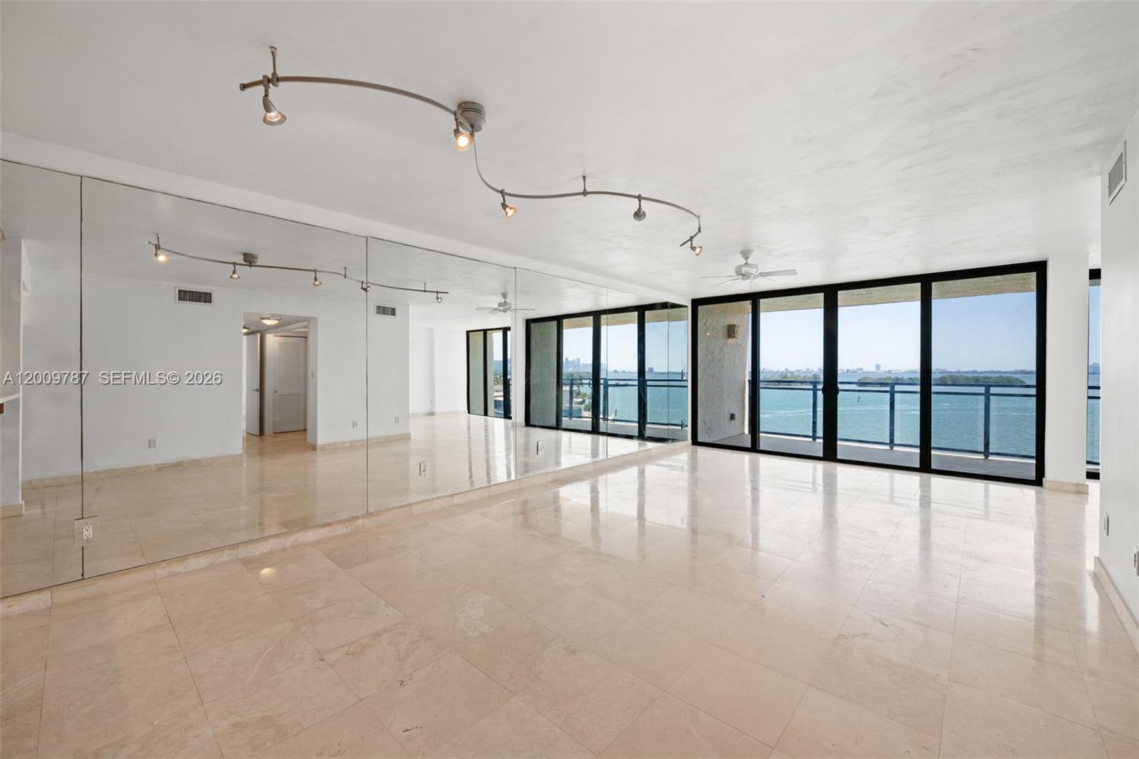 A spacious room features mirrored walls, marble tile flooring, track lighting, and floor-to-ceiling windows — 7751 NE Bayshore Ct # 7B, Miami FL 33138, MIAMI, FL