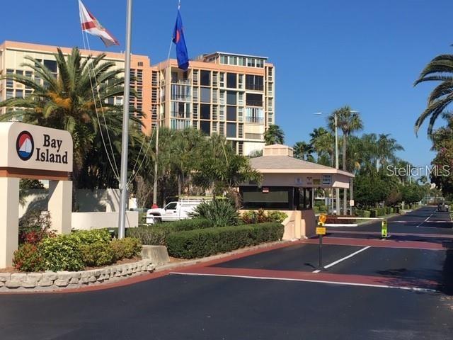 A gated entrance with a Bay Island sign and a guardhouse in front of apartments — 7405 BAY ISLAND DRIVE S UNIT 220, SOUTH PASADENA, FL