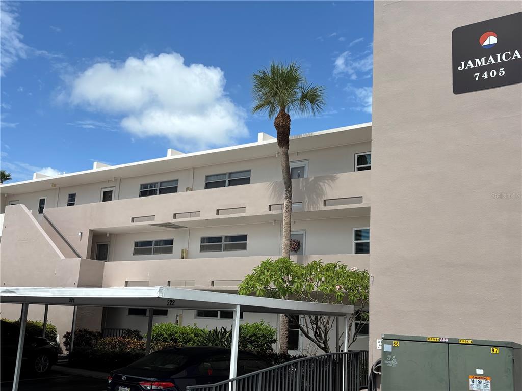 A three-story apartment building exterior features a palm tree and a covered parking area — 7405 BAY ISLAND DRIVE S UNIT 220, SOUTH PASADENA, FL