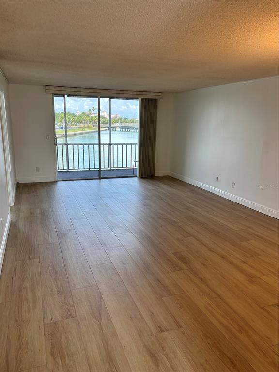 An empty living room features wood-look tile flooring and a sliding glass door overlooking water — 7405 BAY ISLAND DRIVE S UNIT 220, SOUTH PASADENA, FL