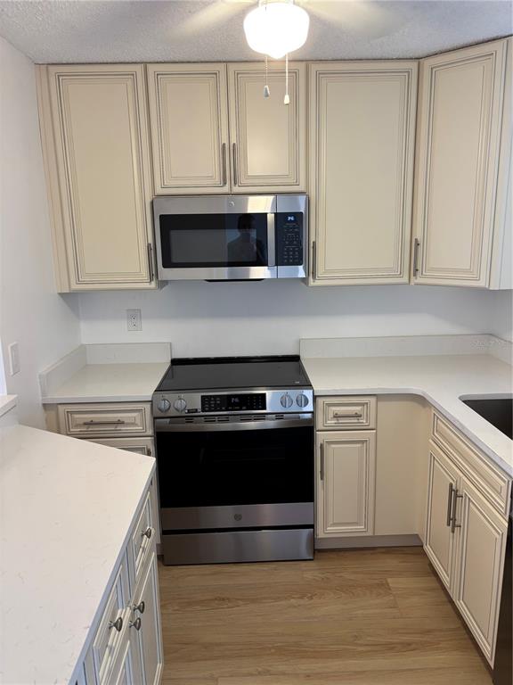 A kitchen features off-white cabinets, stainless steel appliances, and white countertops with wood-look flooring — 7405 BAY ISLAND DRIVE S UNIT 220, SOUTH PASADENA, FL