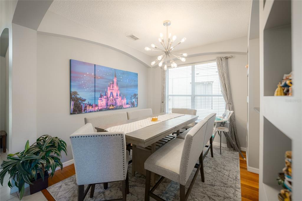 A dining room features a long wooden table, upholstered chairs, a chandelier, and castle artwork — 8663 LA ISLA DRIVE, KISSIMMEE, FL
