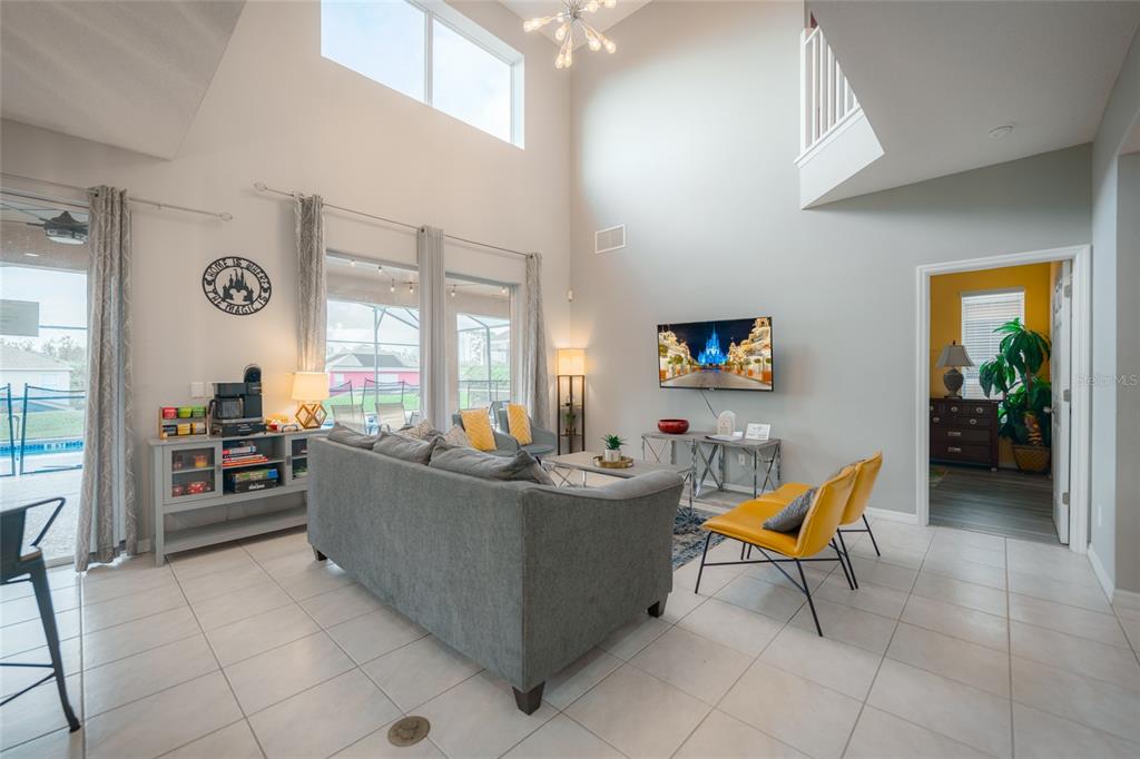 A high-ceilinged living room features a gray sofa, yellow chairs, and a wall-mounted television — 8663 LA ISLA DRIVE, KISSIMMEE, FL