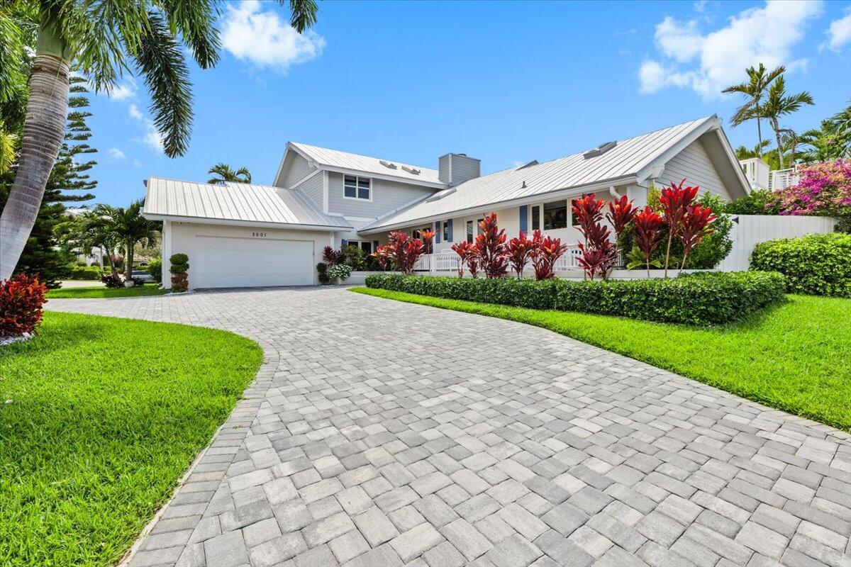 A gray house with a metal roof and a paved driveway sits behind a landscaped yard — 3001 Jasmine Court, Delray Beach FL 33483, DELRAY BEACH, FL