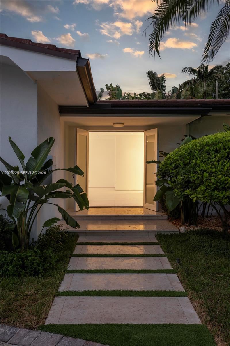 A stone walkway leads to an open double-door entrance of a white house at dusk — 145 S Prospect Dr, Coral Gables FL 33133, CORAL GABLES, FL