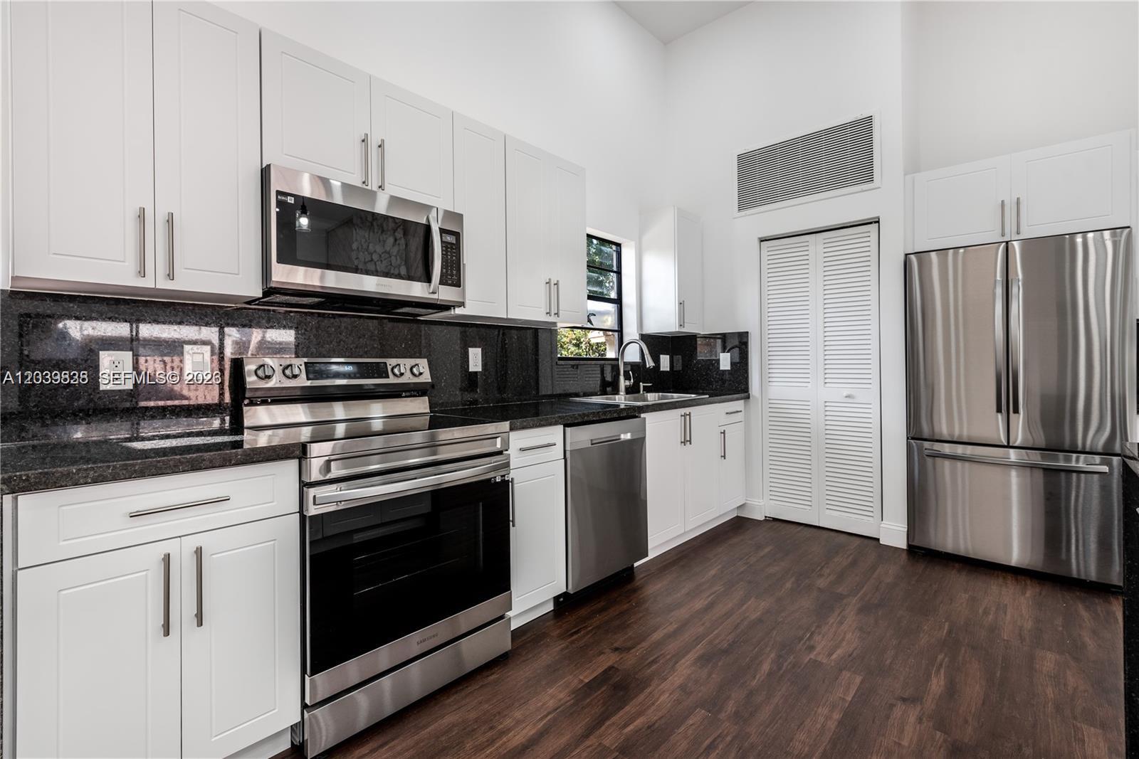 A modern kitchen features white cabinets, stainless steel appliances, and dark granite countertops — 601 Leslie Dr, Hallandale Beach FL 33009, HALLANDALE BEACH, FL