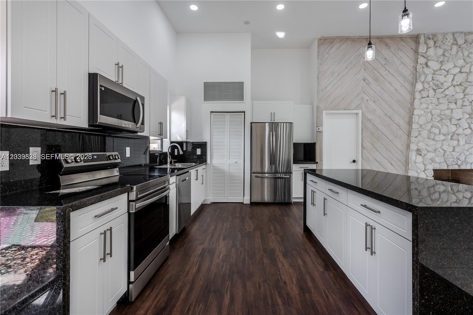 A modern kitchen features white cabinetry, black granite countertops, stainless steel appliances, and wood flooring — 601 Leslie Dr, Hallandale Beach FL 33009, HALLANDALE BEACH, FL