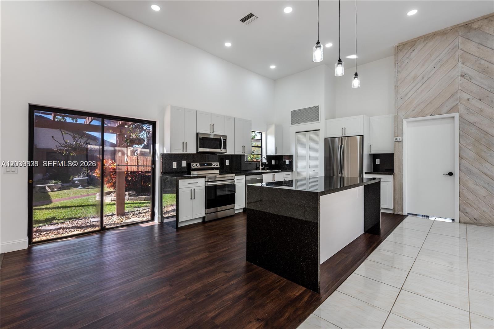A modern kitchen features dark granite countertops, white cabinetry, and a large central island — 601 Leslie Dr, Hallandale Beach FL 33009, HALLANDALE BEACH, FL