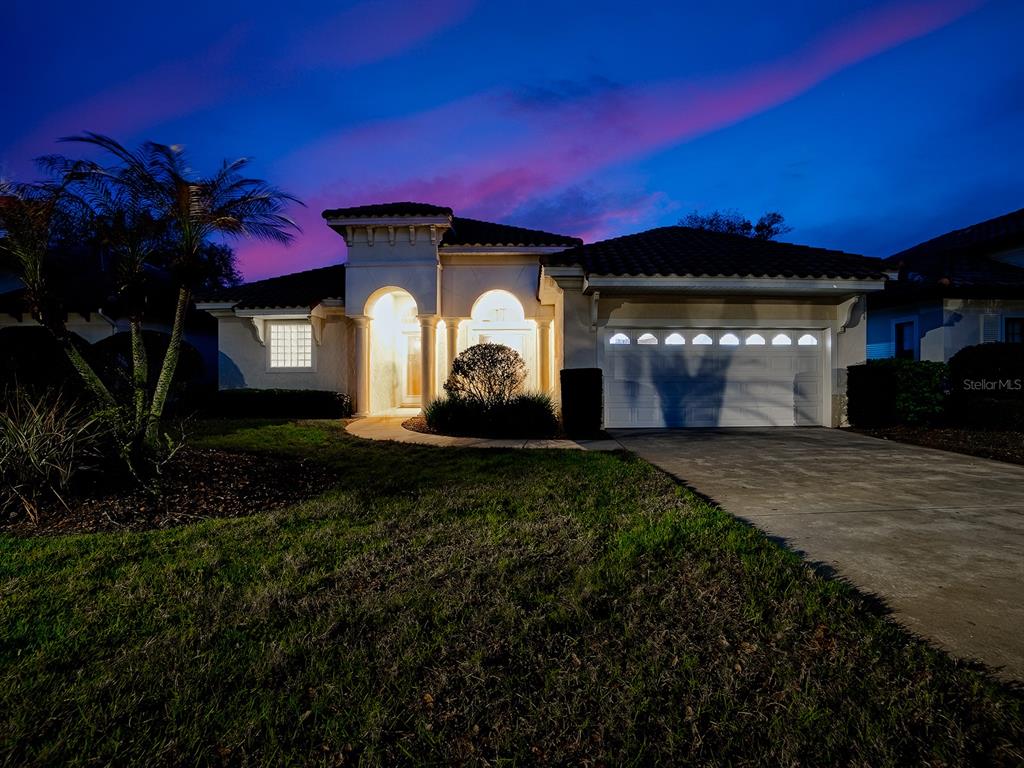 A single-story stucco house with a tile roof and a two-car garage at twilight — 9926 SANTA BARBARA COURT, HOWEY IN THE HILLS, FL