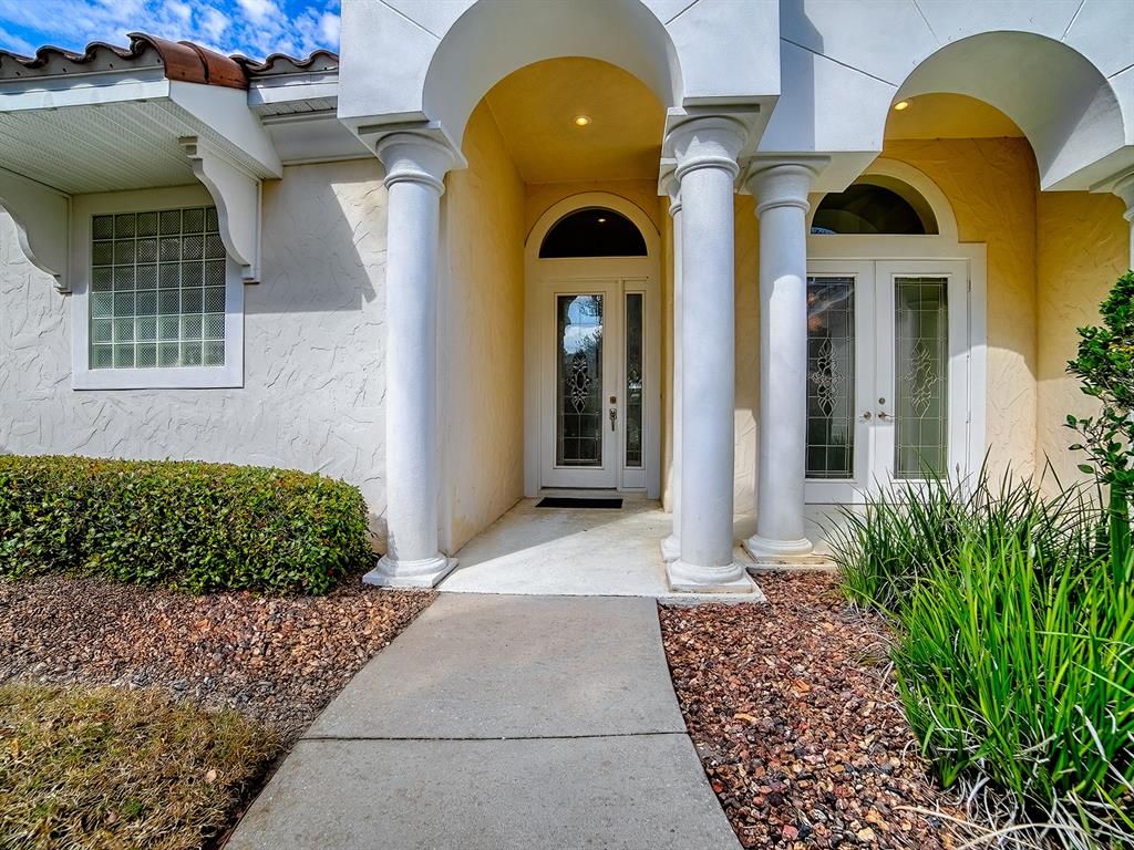 The exterior entrance features a concrete walkway, white columns, and glass-paneled double doors — 9926 SANTA BARBARA COURT, HOWEY IN THE HILLS, FL