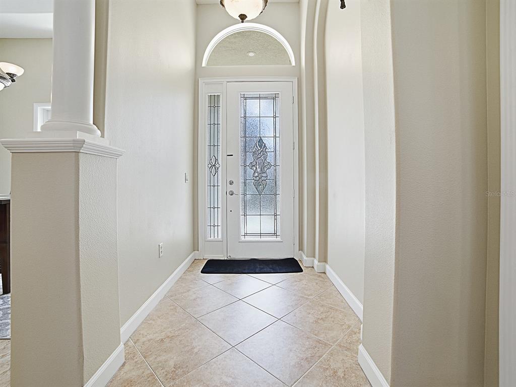 An entryway features a decorative glass front door, arched transom window, and tiled flooring — 9926 SANTA BARBARA COURT, HOWEY IN THE HILLS, FL