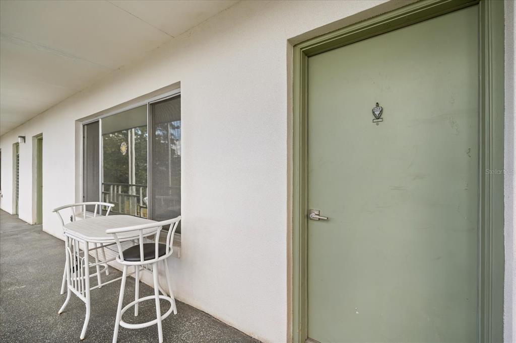 A white exterior walkway features a green door, a window, and a small bistro set — 1700 6TH STREET NW UNIT B24, WINTER HAVEN, FL