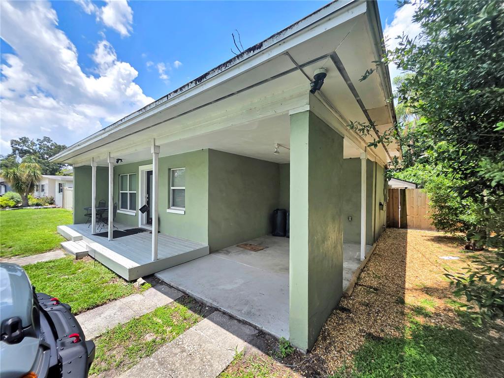 A green house exterior features a covered concrete carport and an adjacent wooden front porch — 5117 LAKE HOWELL ROAD, WINTER PARK, FL