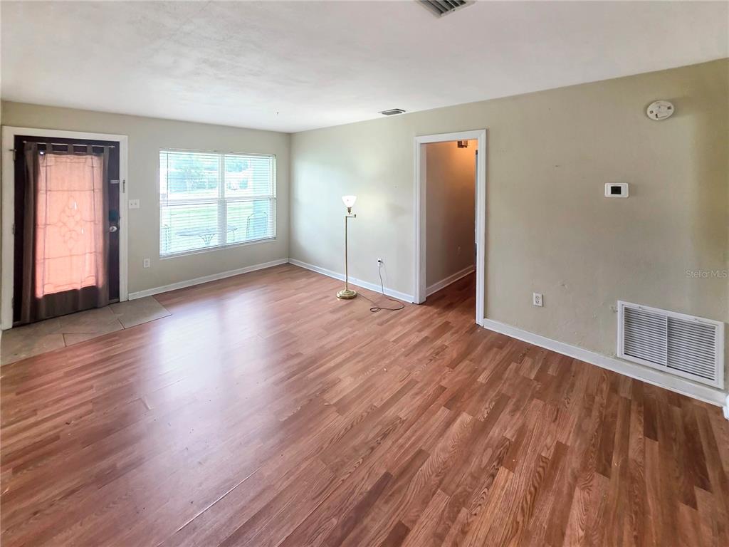 An empty living room features wood-look flooring, light-colored walls, a window, and a doorway — 5117 LAKE HOWELL ROAD, WINTER PARK, FL