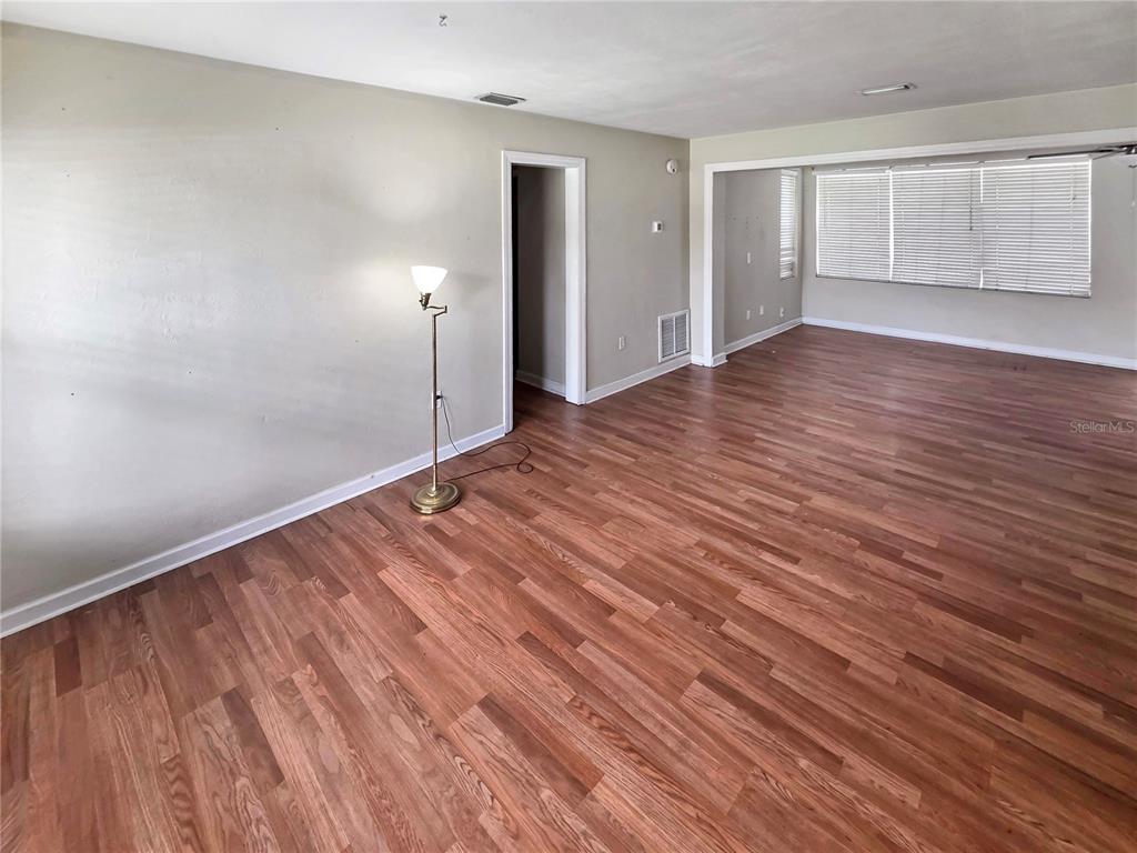 An empty room features light-colored walls, wood-look flooring, a floor lamp, and large windows — 5117 LAKE HOWELL ROAD, WINTER PARK, FL