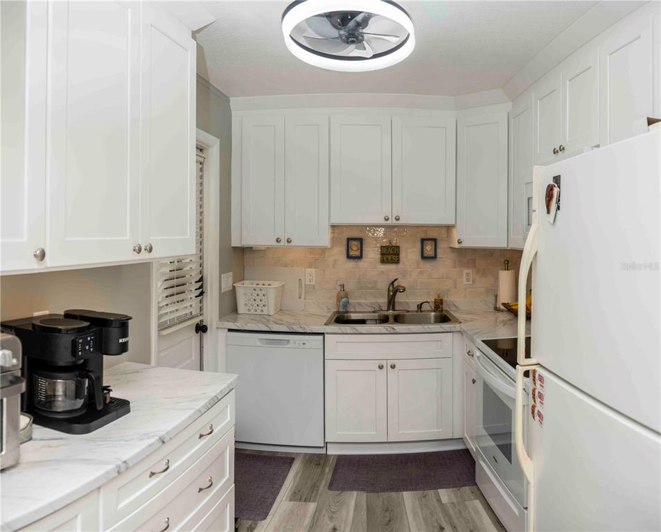 A kitchen features white cabinets, marble-look countertops, a double sink, and stainless steel appliances — 6024 CORAL WAY, BRADENTON, FL