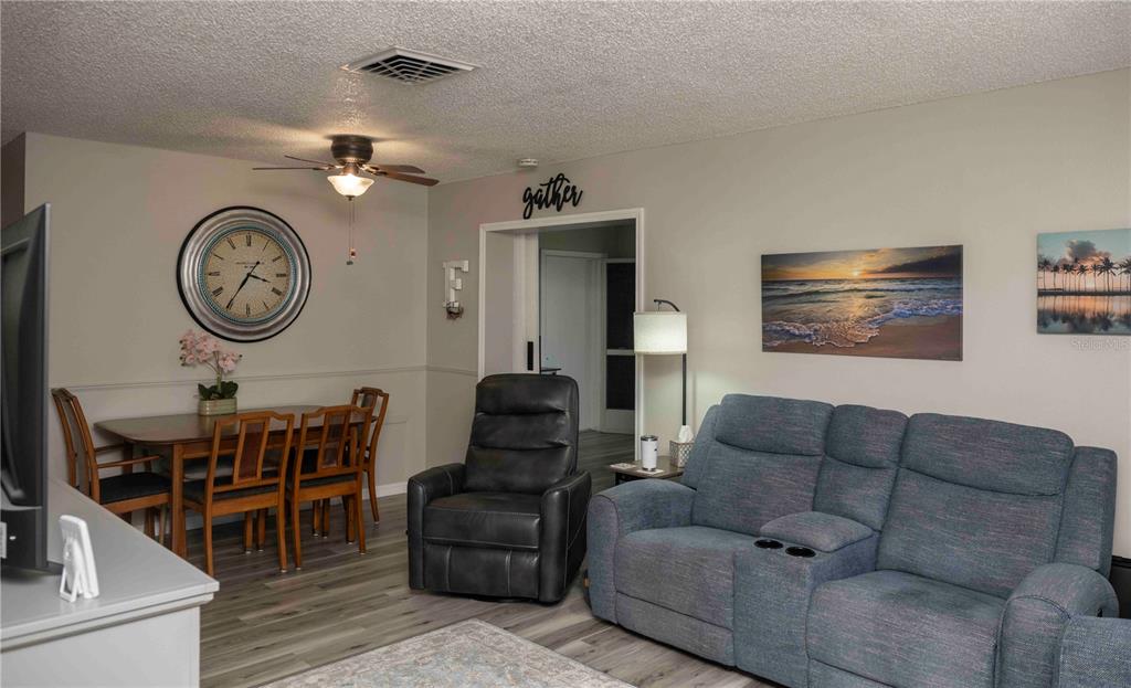A living and dining area features gray flooring, a blue reclining sofa, and a dining set — 6024 CORAL WAY, BRADENTON, FL