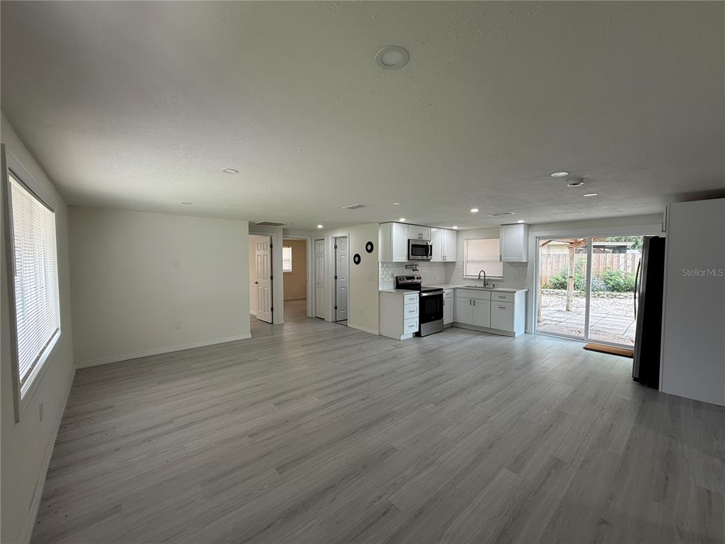 An open-concept living area features light wood-look flooring, white walls, and a modern kitchen — 4553 EDITH STREET, NEW PORT RICHEY, FL