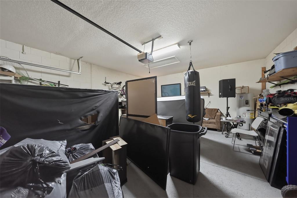 A cluttered garage features a hanging punching bag, storage items, and a concrete floor — 2772 BIG TIMBER DRIVE, KISSIMMEE, FL