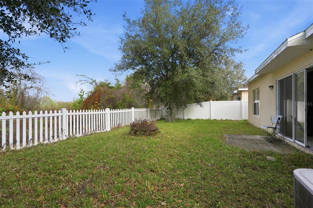 A backyard with a white picket fence, a large tree, and a concrete patio area — 2772 BIG TIMBER DRIVE, KISSIMMEE, FL