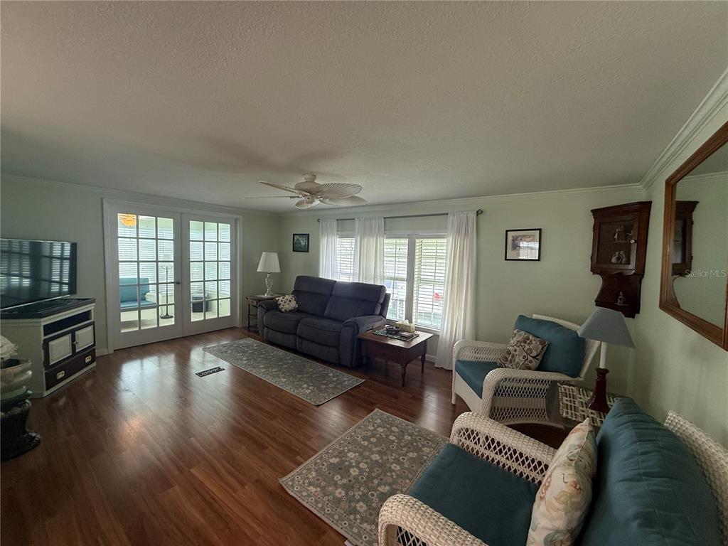 A living room features hardwood floors, a gray sofa, two wicker chairs, and French doors — 6100 62ND AVENUE N UNIT 71, PINELLAS PARK, FL