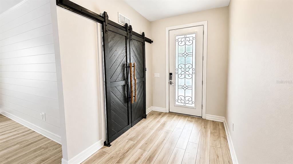 An entryway features light wood-look flooring, a white front door, and black sliding barn doors — 10903 GREEN HARVEST DRIVE, RIVERVIEW, FL