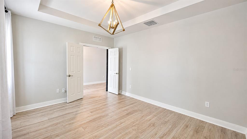 A bedroom with light wood-look flooring, a tray ceiling, and a gold geometric chandelier — 10903 GREEN HARVEST DRIVE, RIVERVIEW, FL