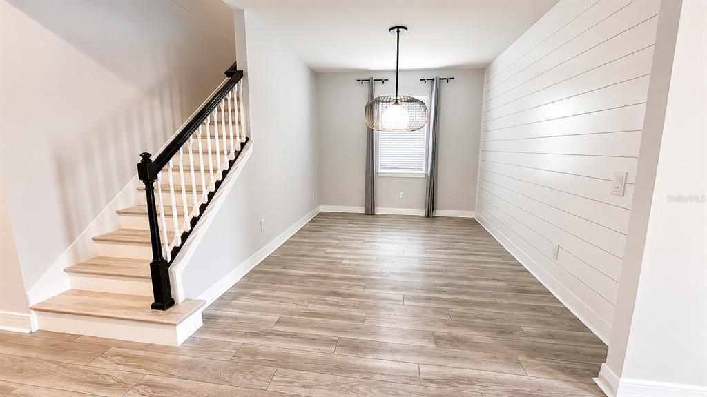 A dining area features wood-look flooring, a shiplap wall, and a staircase with a black railing — 10903 GREEN HARVEST DRIVE, RIVERVIEW, FL