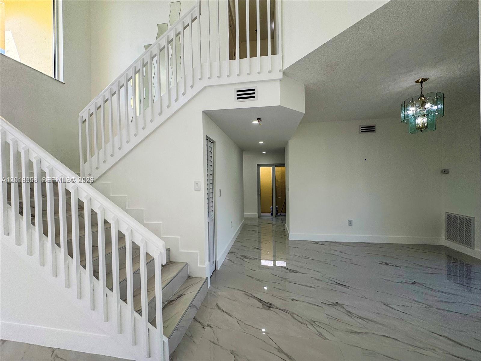 A bright foyer features a white staircase, marble-look tile flooring, and a decorative chandelier — 15428 SW 50th Ter # 0, Miami FL 33185, MIAMI, FL