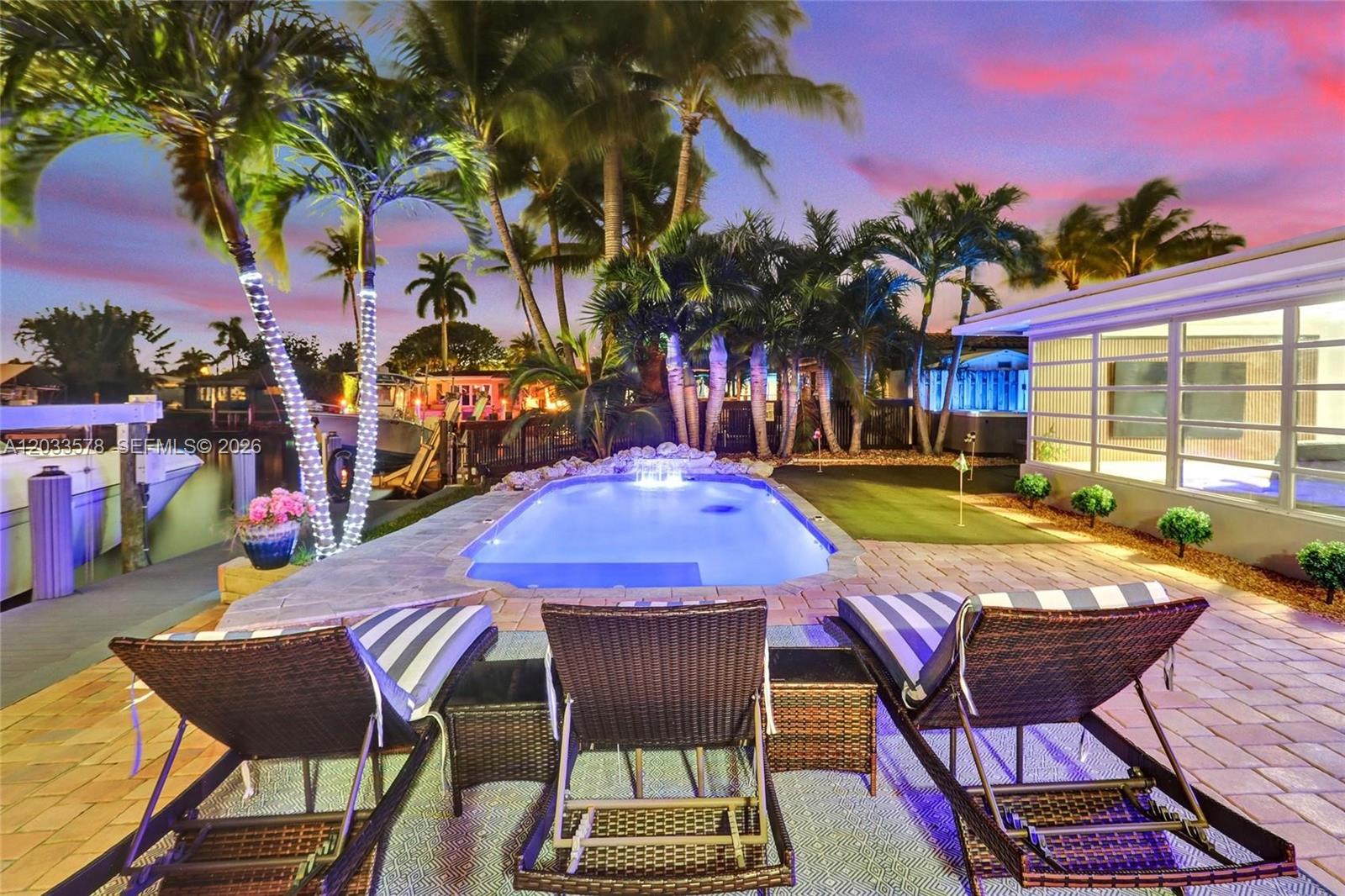 A backyard patio features a swimming pool, lounge chairs, palm trees, and a putting green — 200 SE 3rd St, Pompano Beach FL 33060, POMPANO BEACH, FL