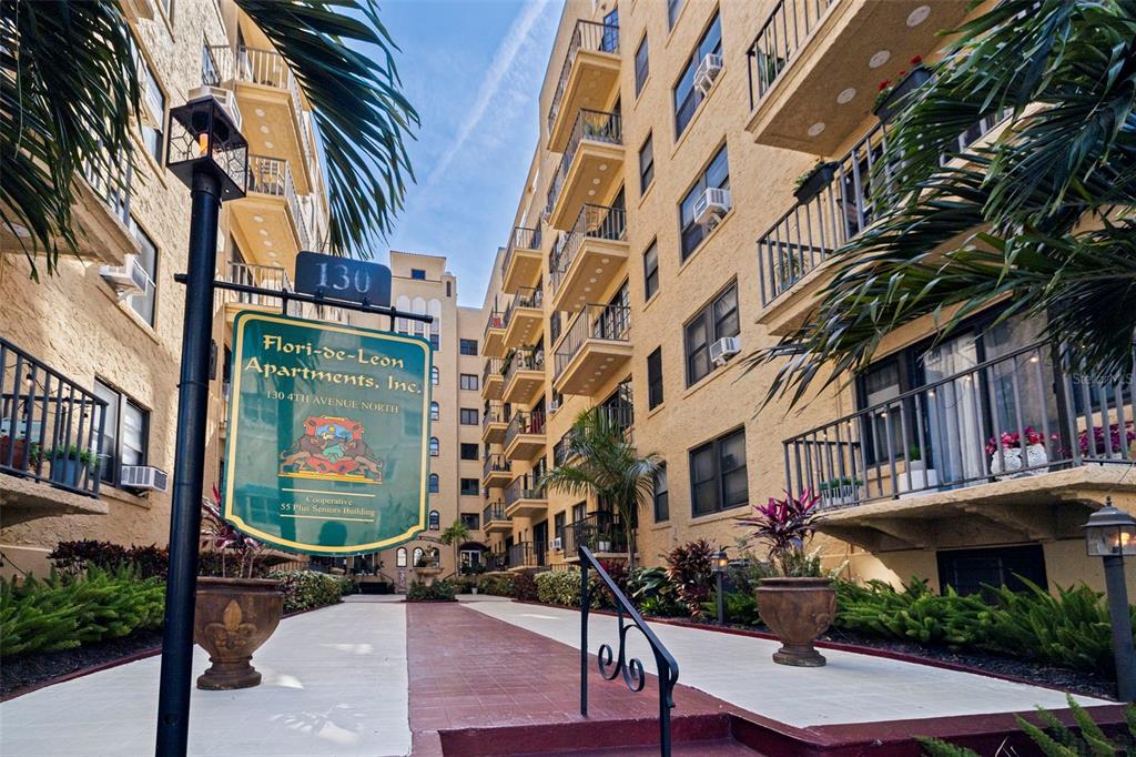A sign for the Flori-de-Leon Apartments stands in a courtyard between two yellow buildings — 130 4TH AVENUE N UNIT 602, ST PETERSBURG, FL