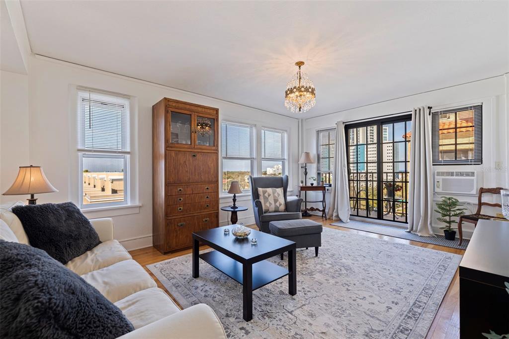 A living room features a white sofa, a wooden armoire, a chandelier, and a balcony door — 130 4TH AVENUE N UNIT 602, ST PETERSBURG, FL