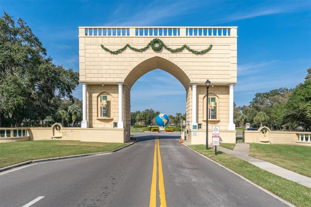 A large, beige, arched stone gate stands over a road leading toward a globe sculpture — 2461 RHODESIAN DRIVE UNIT 45, CLEARWATER, FL