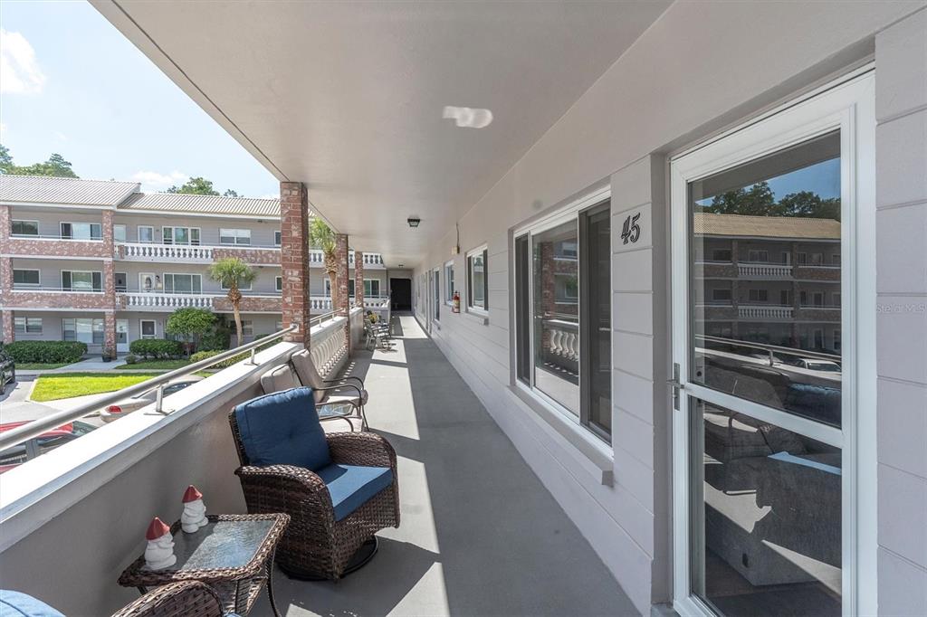 An outdoor balcony walkway features wicker chairs, a small table, and unit number 45 — 2461 RHODESIAN DRIVE UNIT 45, CLEARWATER, FL