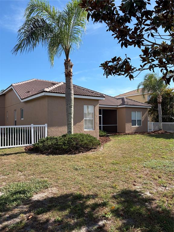 The exterior of a tan stucco house features a palm tree and a white fence — 7779 AROLLA PINE BOULEVARD, SARASOTA, FL